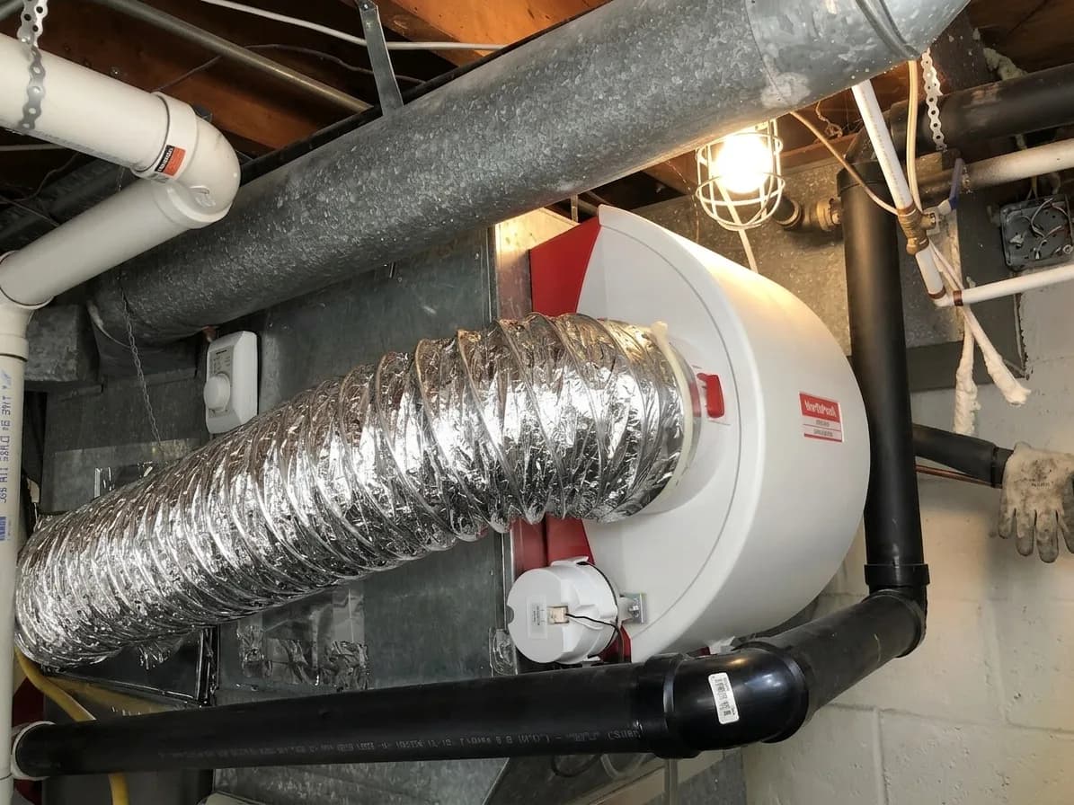 Heat recovery ventilator mounted to a basement ceiling with insulated ducts.